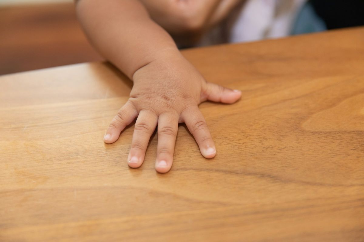 Een babyhandje op een houten tafel
