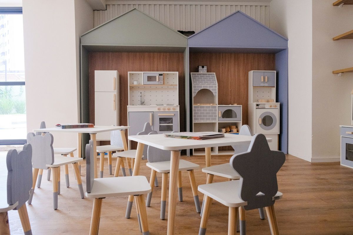 Een speelruimte met kleine tafels en speelkeukens in de vorm van een huisje
