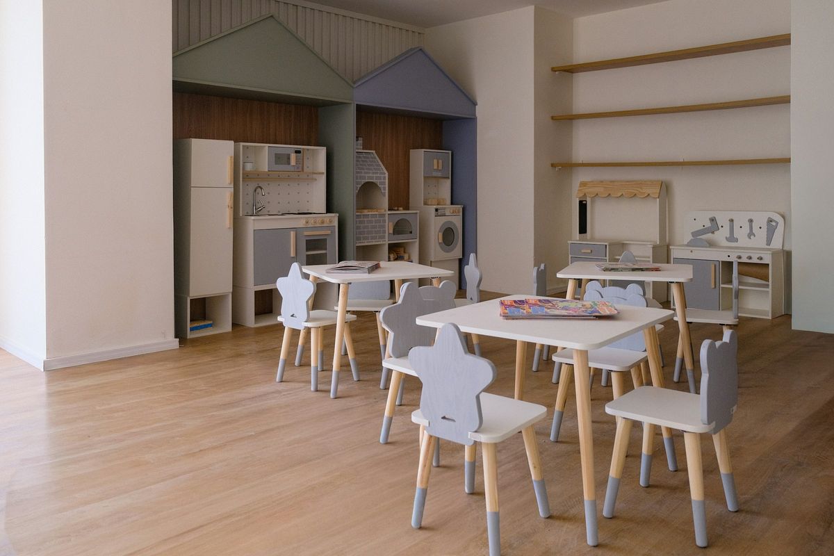Een lichte speelruimte met kleine tafels, stoeltjes in de vorm van een ster en speelkeukens in de vorm van een huisje